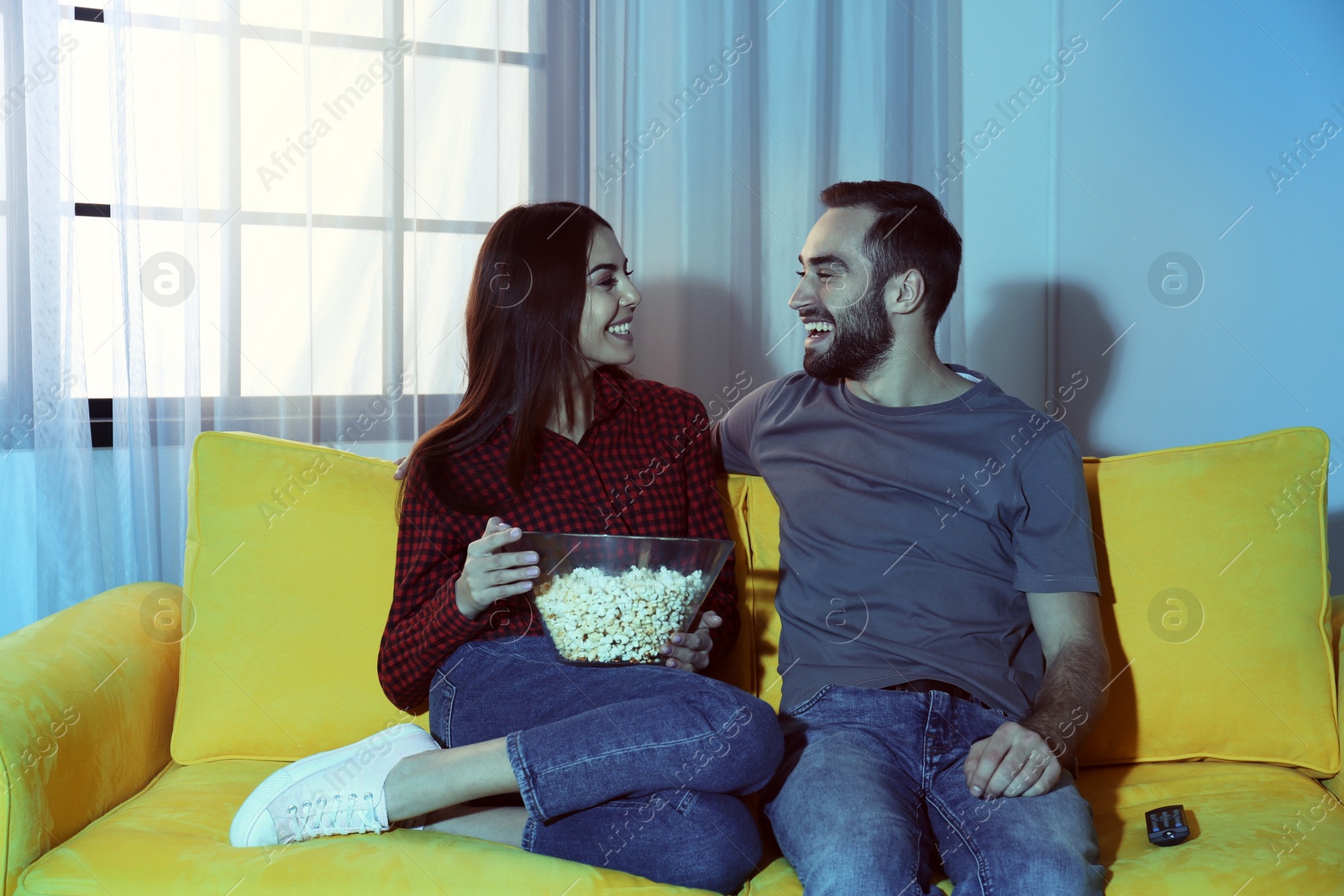 Photo of Happy young couple watching TV on sofa at home