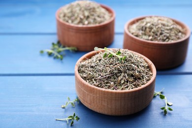 Photo of Bowls with dried and fresh thyme on blue wooden table, closeup