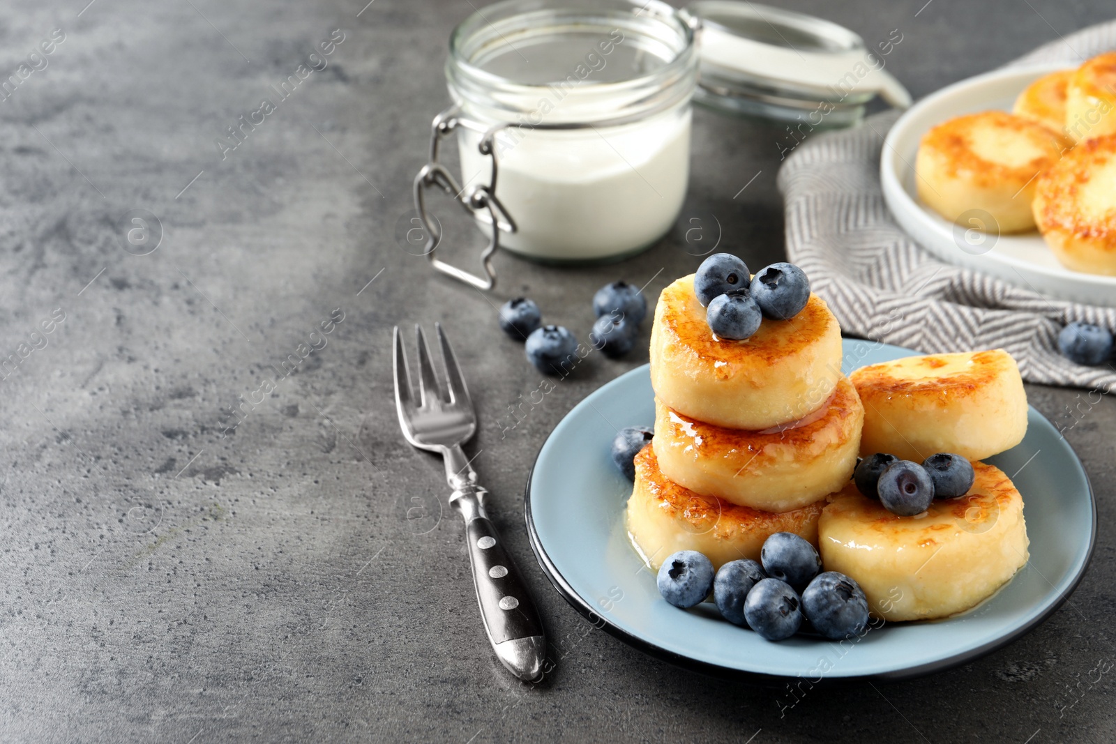 Photo of Delicious cottage cheese pancakes with blueberries and honey on grey table, space for text