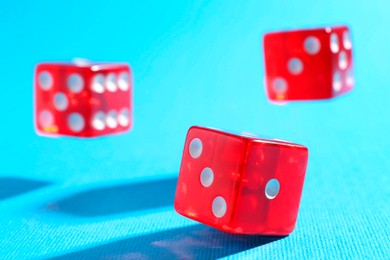 Photo of Three red game dices falling on light blue background, closeup