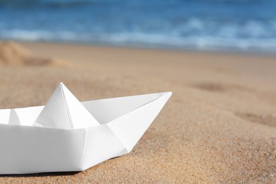 Photo of White paper boat near sea on sunny day, closeup. Space for text