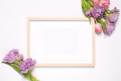 Photo of Empty photo frame and beautiful tulip flowers on white background, flat lay. Mockup for design