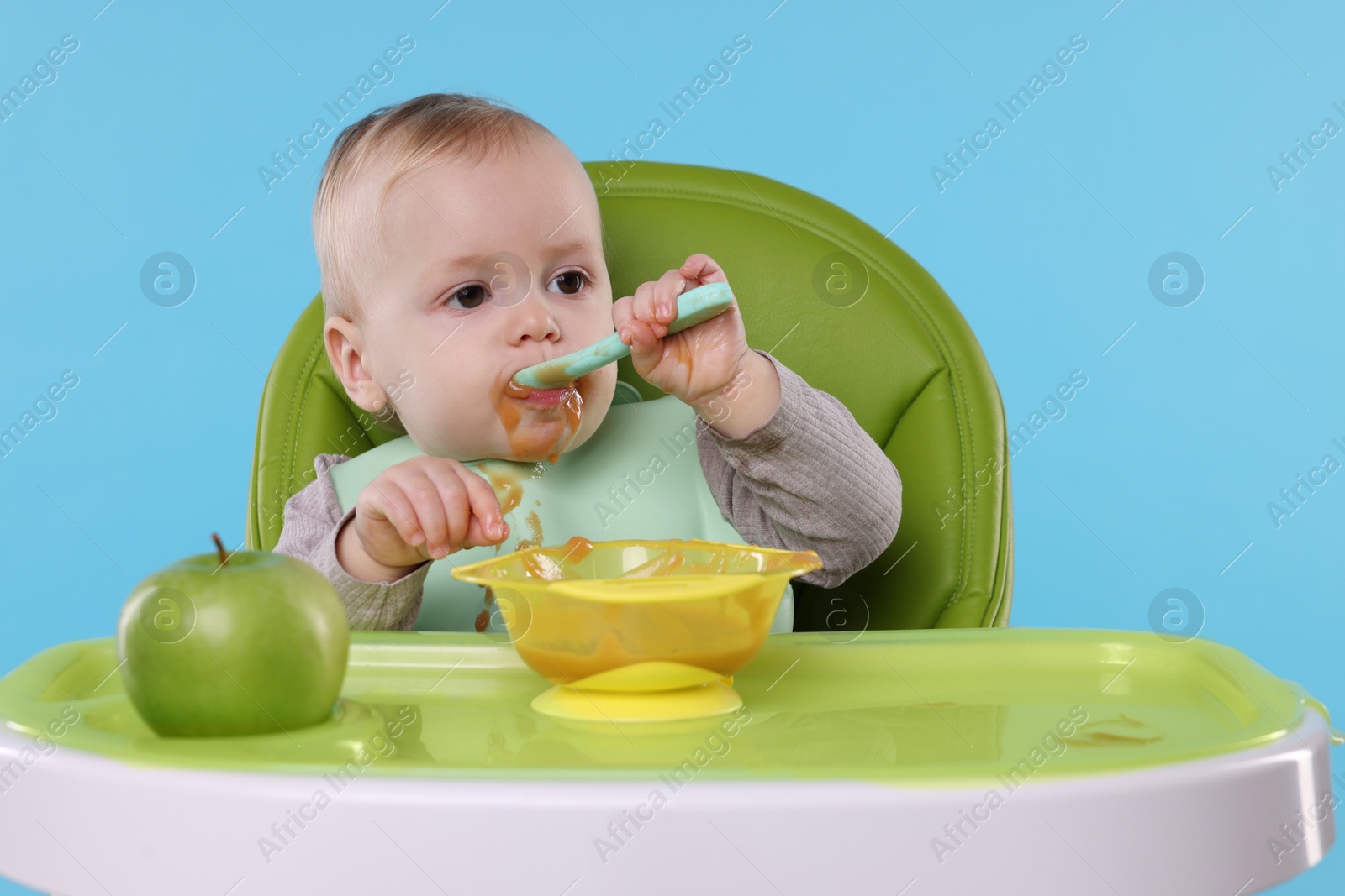 Photo of Cute little baby eating healthy food in high chair on light blue background