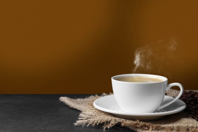 Image of Cup of hot aromatic coffee and roasted beans on black table against brown background. Space for text
