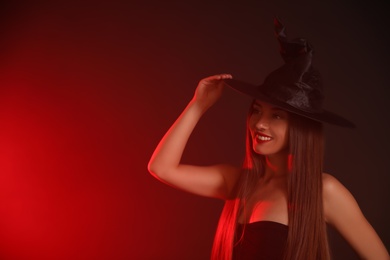 Young woman wearing witch costume on dark background, space for text. Halloween party