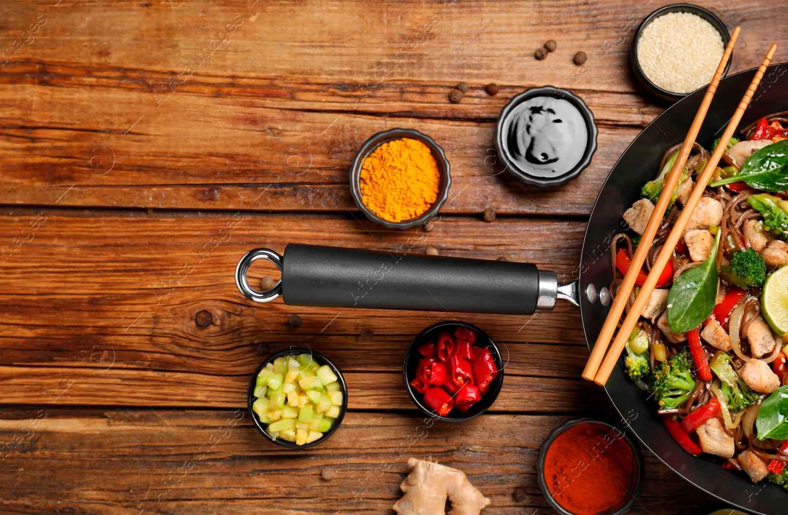 Photo of Stir-fry. Tasty noodles with meat in wok, chopsticks and ingredients on wooden table, flat lay. Space for text