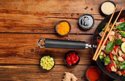 Stir-fry. Tasty noodles with meat in wok, chopsticks and ingredients on wooden table, flat lay. Space for text