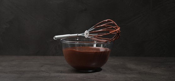 Bowl and whisk with yummy chocolate cream on black table. Banner design