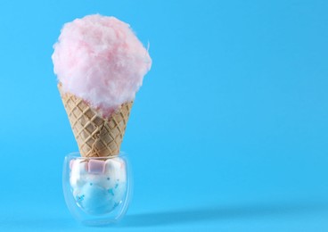 Photo of Sweet cotton candy in waffle cone and marshmallows on light blue background. Space for text