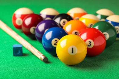Many colorful billiard balls, cue and chalk on green table, closeup