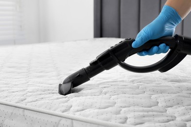 Photo of Woman disinfecting mattress with vacuum cleaner indoors, closeup