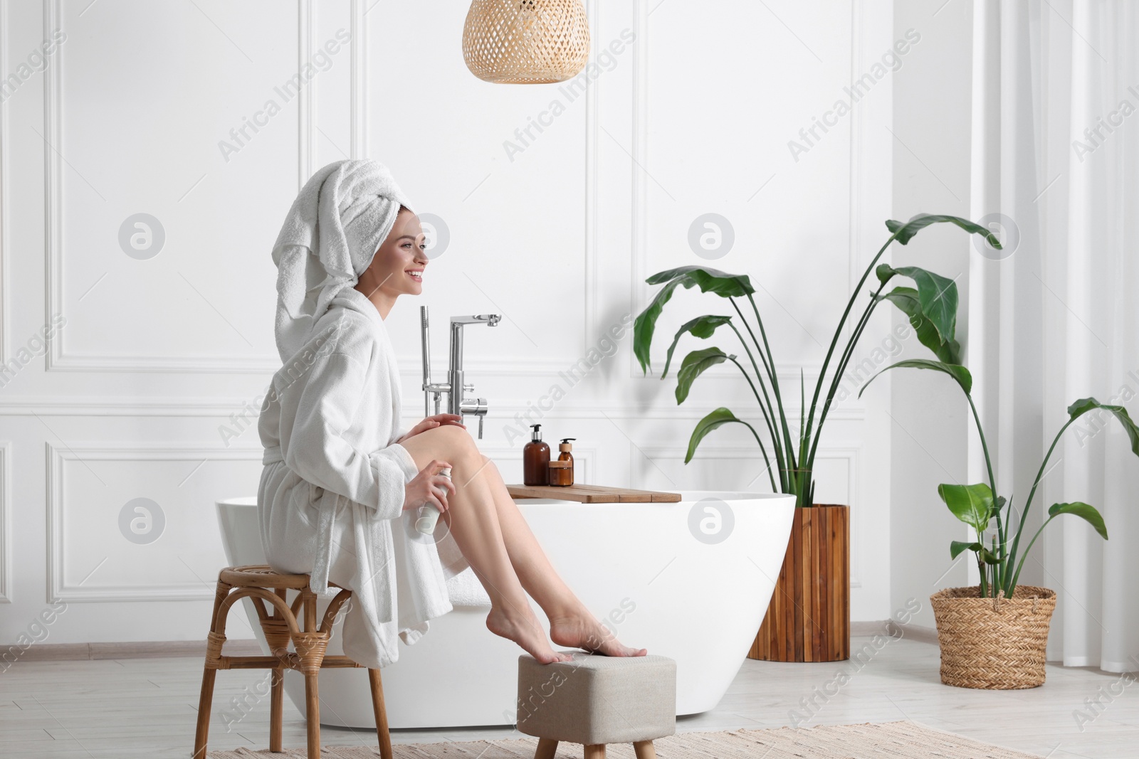 Photo of Beautiful young woman applying body spray onto legs in bathroom, space for text