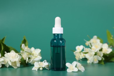 Photo of Essential oil in bottle and beautiful jasmine flowers on green background