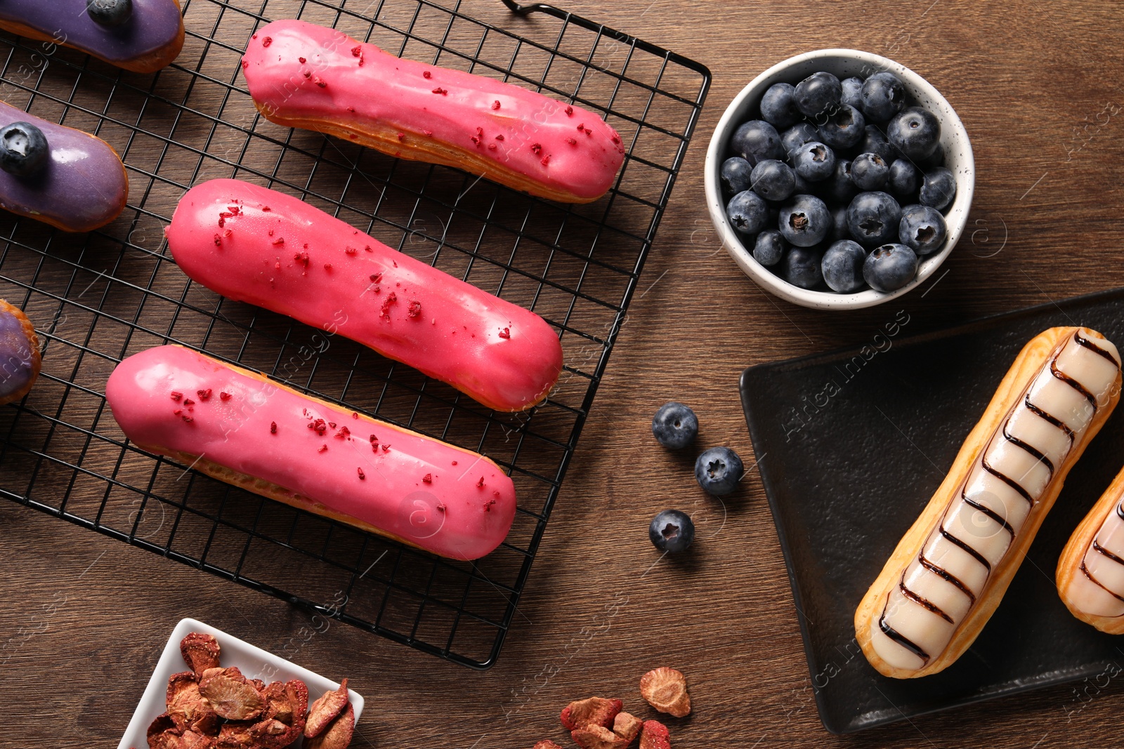 Photo of Tasty glazed eclairs and blueberries on wooden table, flat lay