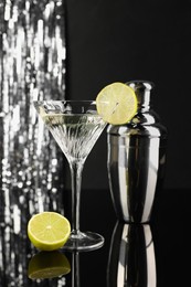 Photo of Martini cocktail with lemon slice and shaker on black and silver background