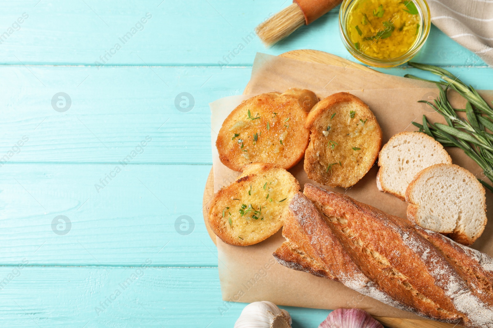 Photo of Slices of toasted bread with garlic and herbs on light blue wooden table, flat lay. Space for text