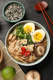 Photo of Bowl of delicious ramen, ingredients and chopsticks on black table, flat lay. Noodle soup