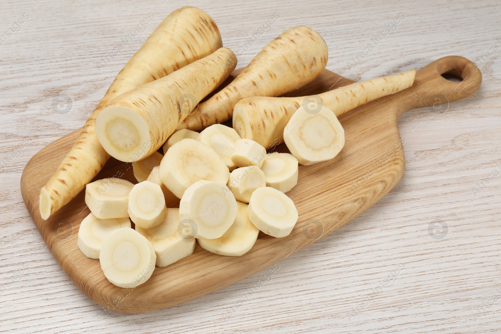 Photo of Whole and cut fresh ripe parsnips on white wooden table