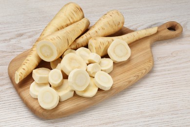 Photo of Whole and cut fresh ripe parsnips on white wooden table