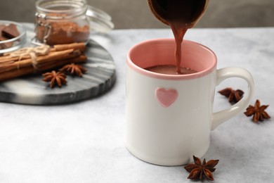 Photo of Pouring tasty hot chocolate into cup at light table, closeup. Space for text