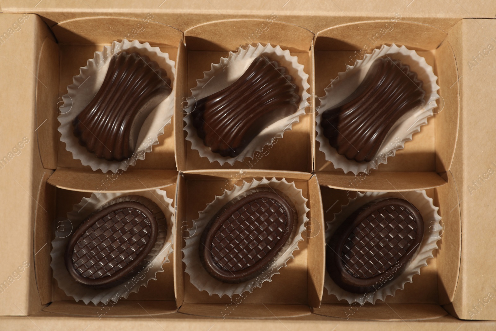 Photo of Many delicious chocolate candies in box, top view. Production line
