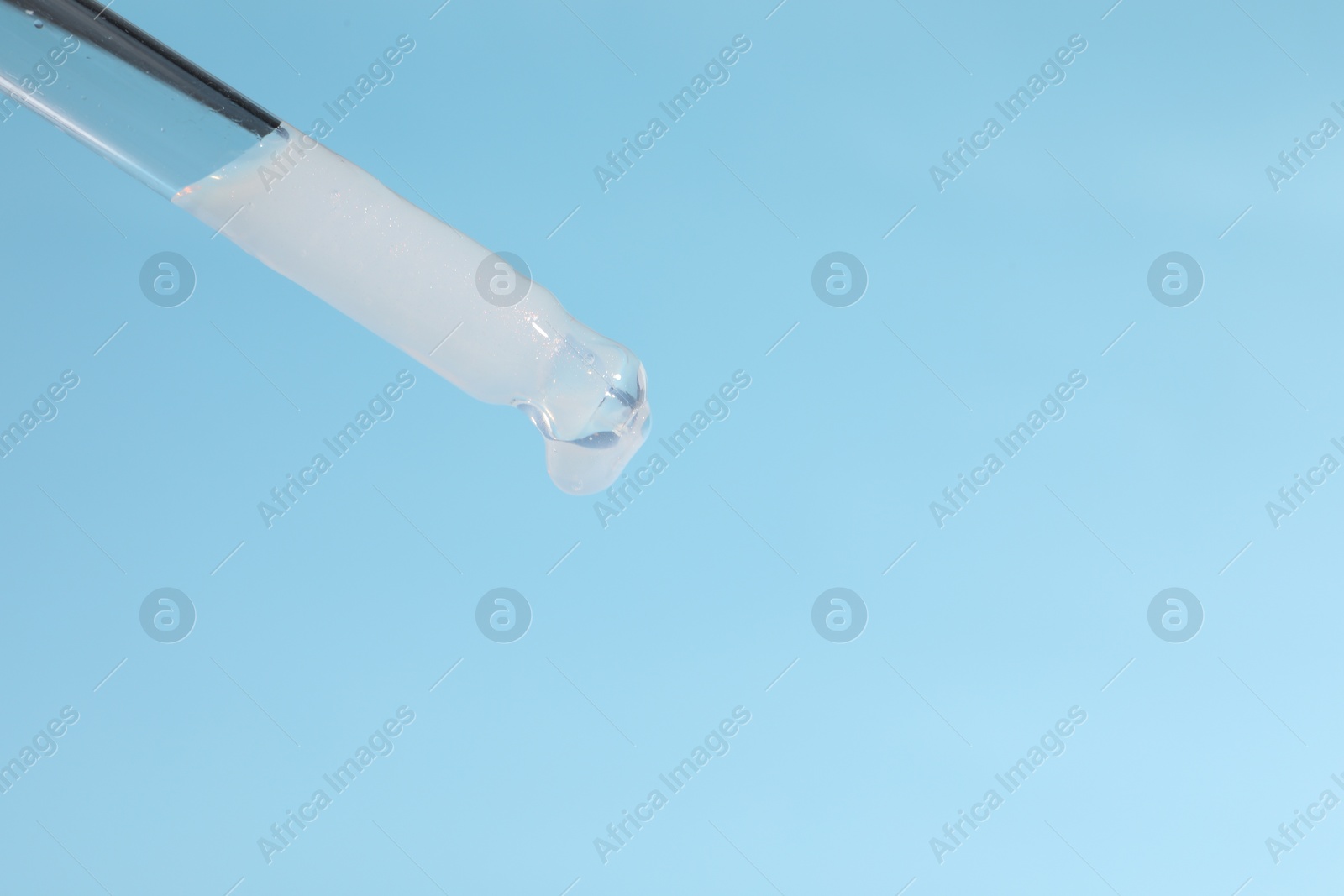 Photo of Dripping cosmetic serum from pipette on light blue background, closeup. Space for text