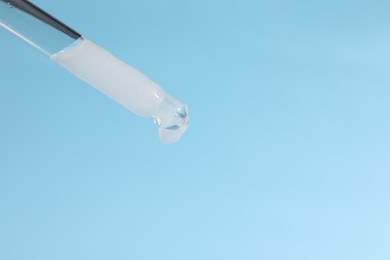 Photo of Dripping cosmetic serum from pipette on light blue background, closeup. Space for text