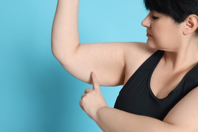 Photo of Obese woman with flabby arm on light blue background. Weight loss surgery