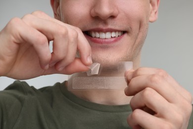 Young man with whitening strips on light grey background, closeup