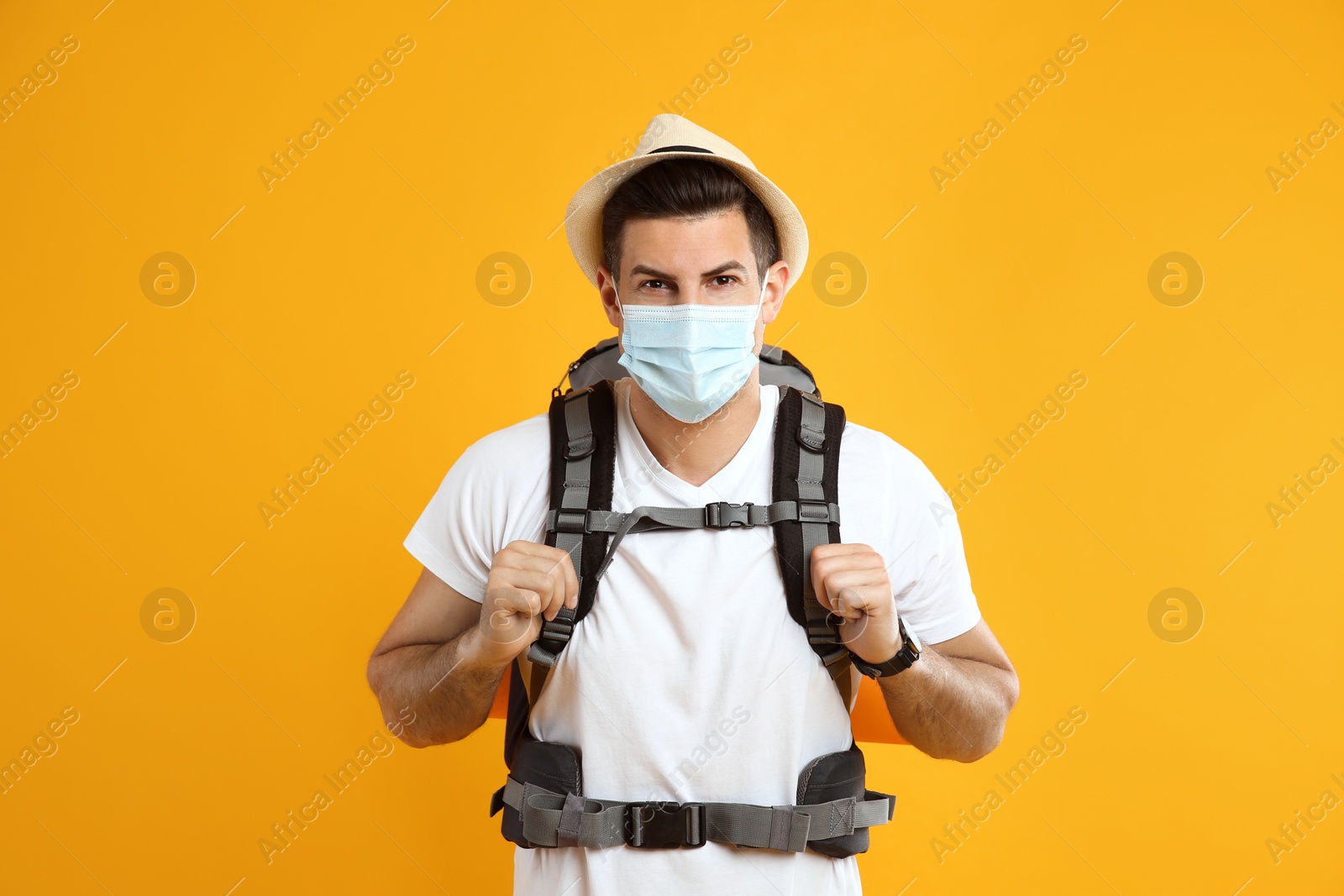 Photo of Male tourist in protective mask with travel backpack on yellow background
