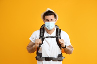 Photo of Male tourist in protective mask with travel backpack on yellow background