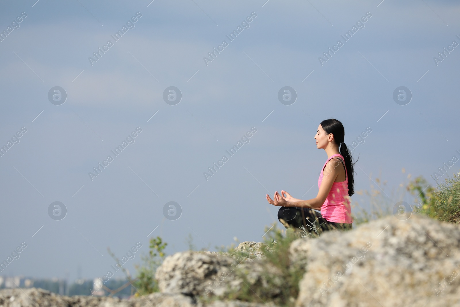 Photo of Young woman meditating on cliff. Space for text