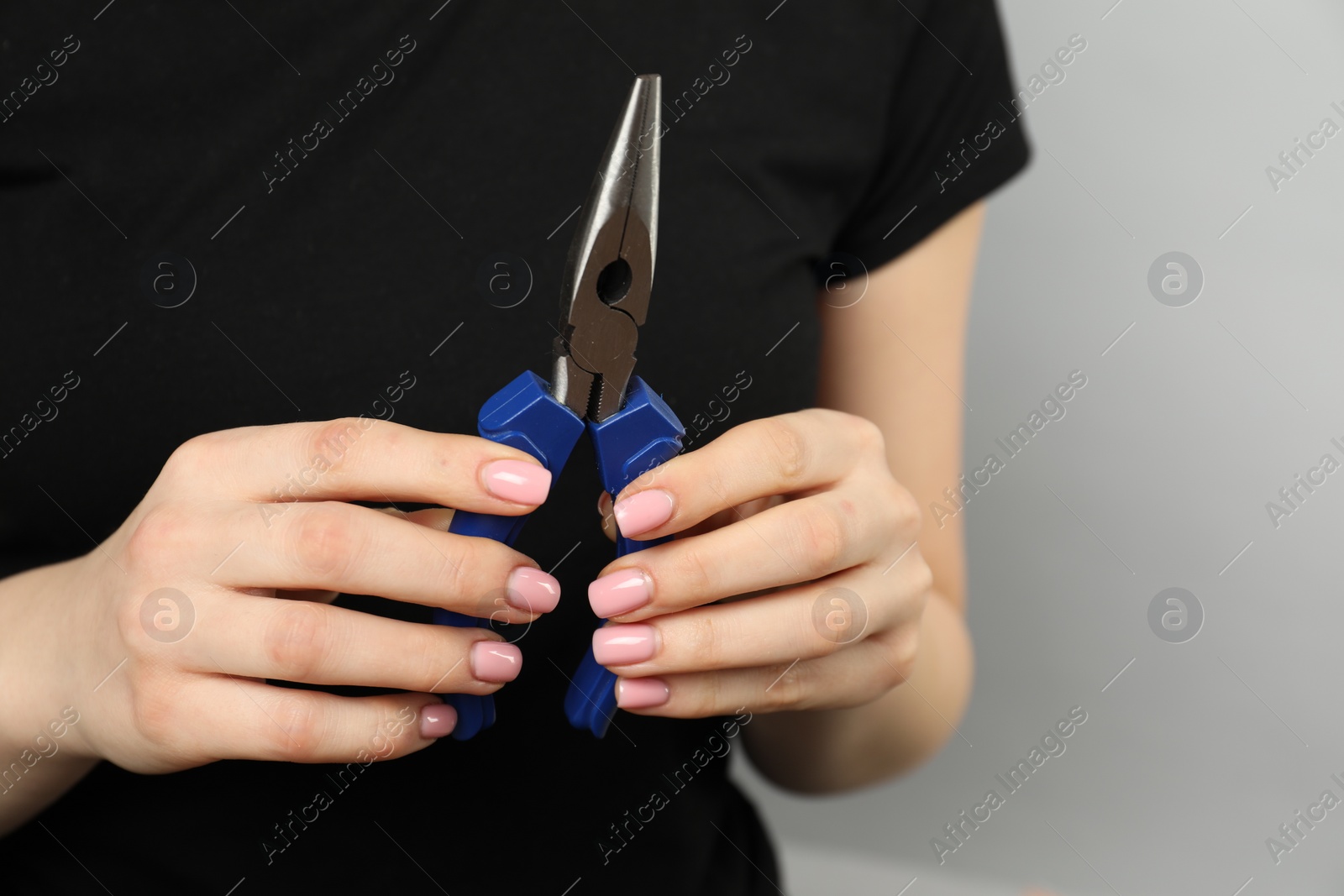 Photo of Woman with needle nose pliers on grey background, closeup. Space for text