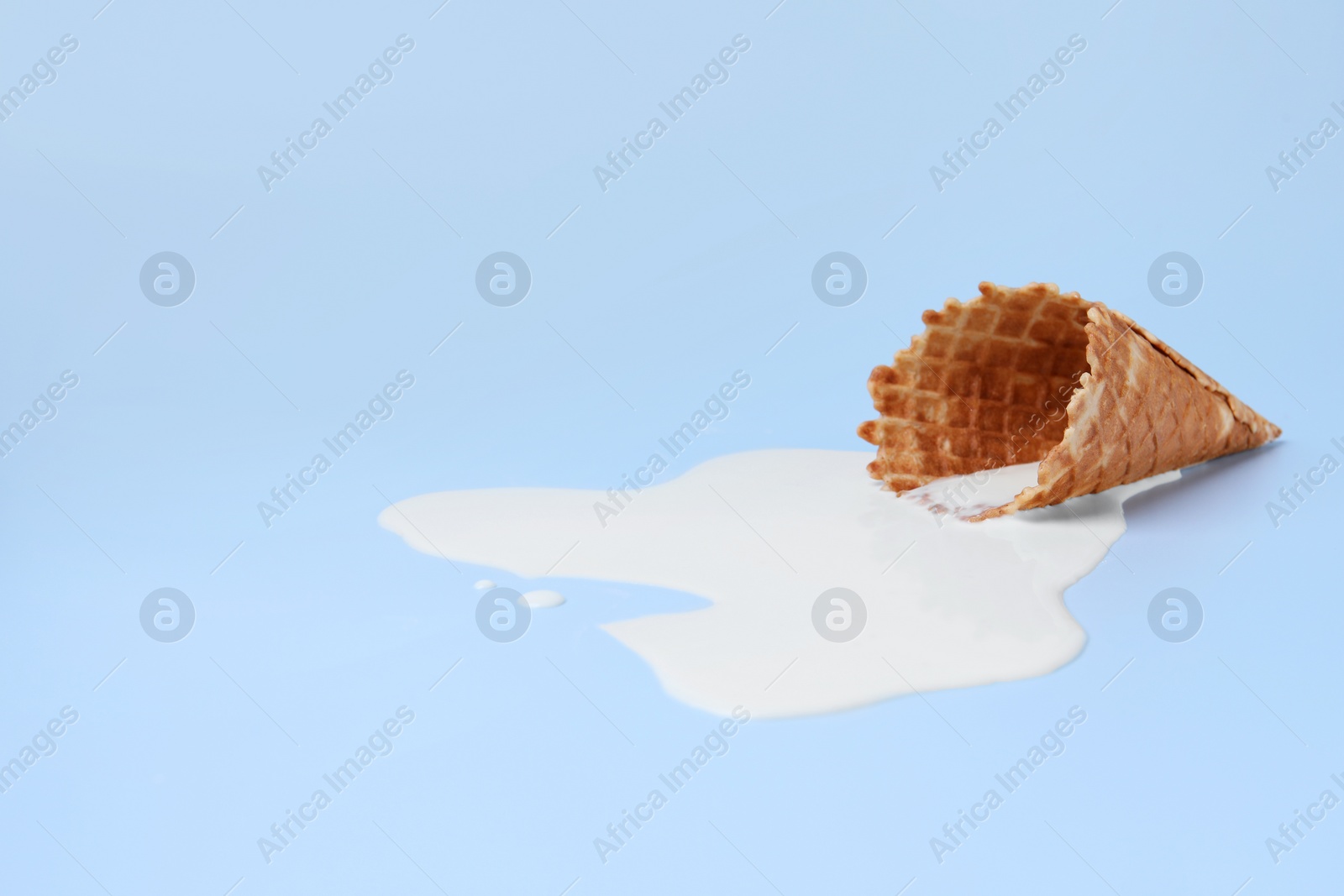 Photo of Melted ice cream and wafer cone on light blue background, space for text