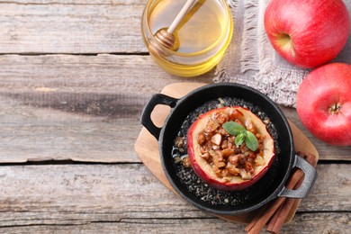 Photo of Tasty baked apple with nuts in baking dish, honey and cinnamon sticks on wooden table, flat lay. Space for text