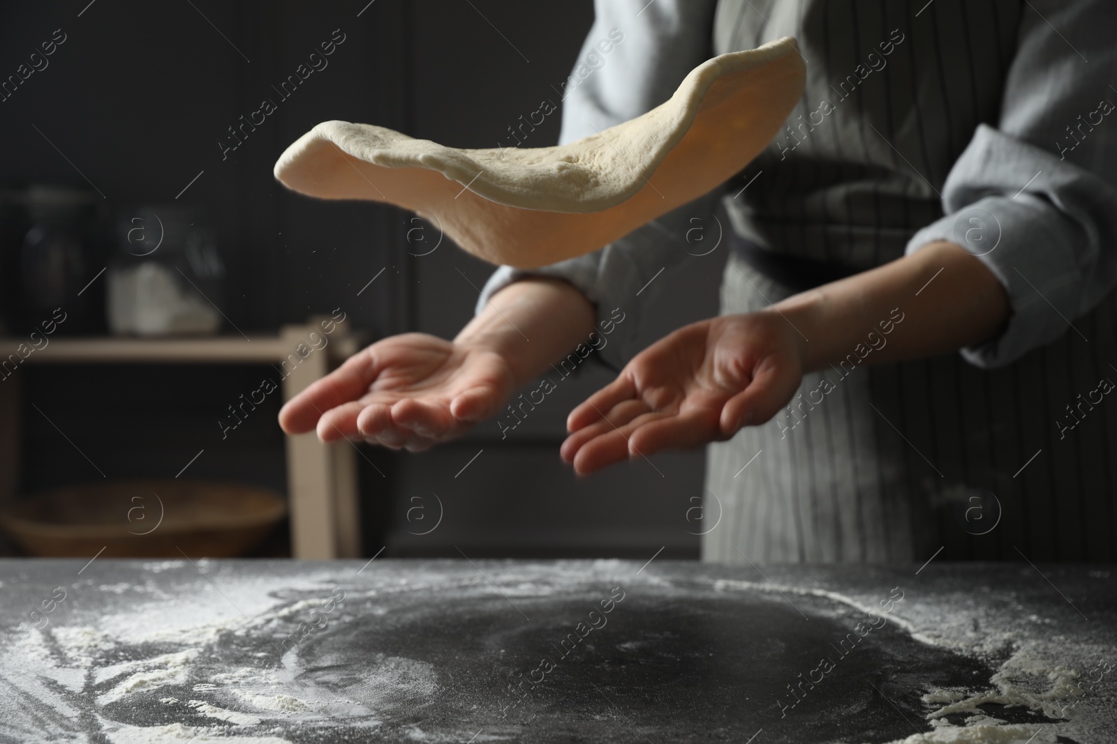 Photo of Woman tossing pizza dough at table in kitchen, closeup