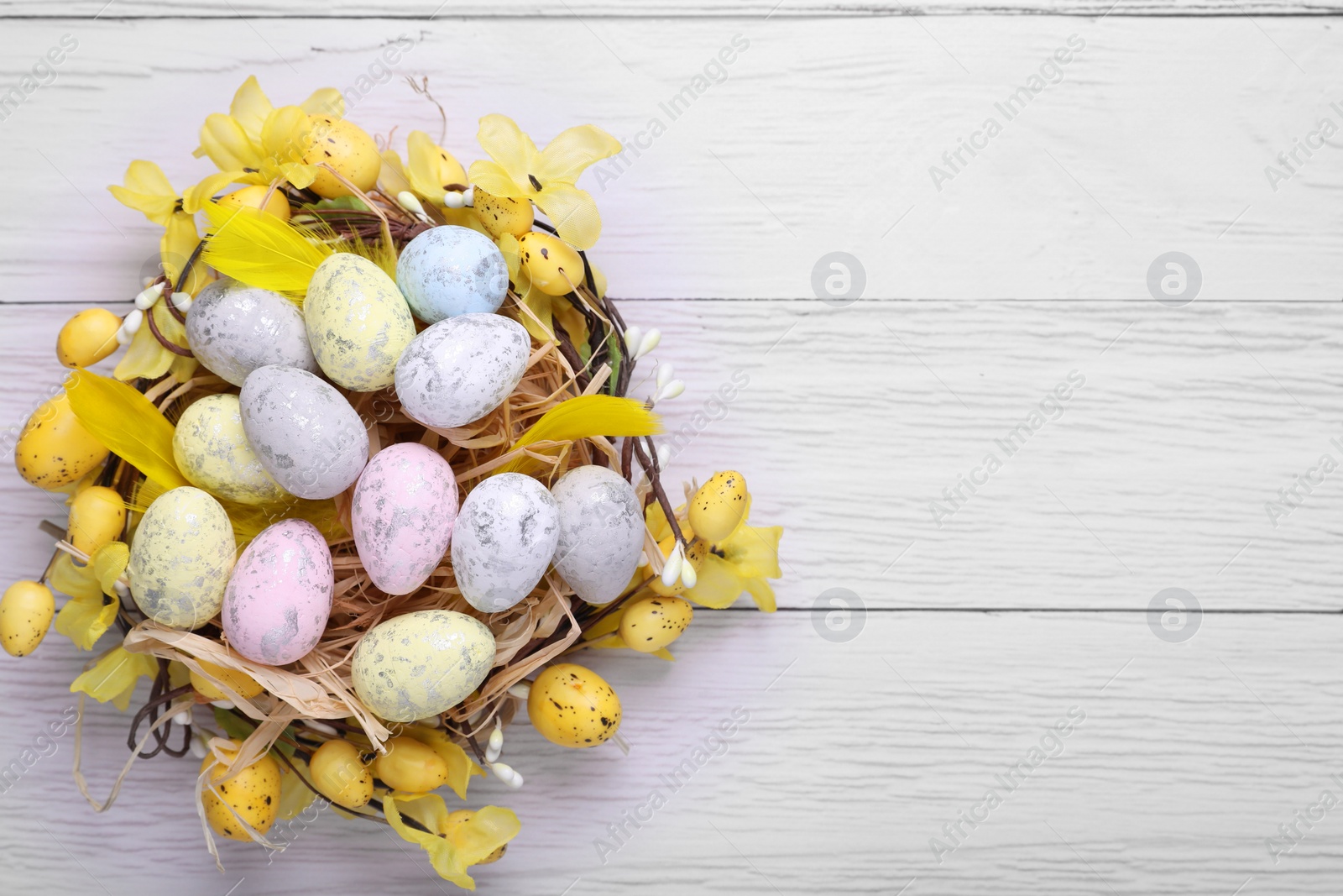 Photo of Festively decorated Easter eggs on white wooden table, top view. Space for text