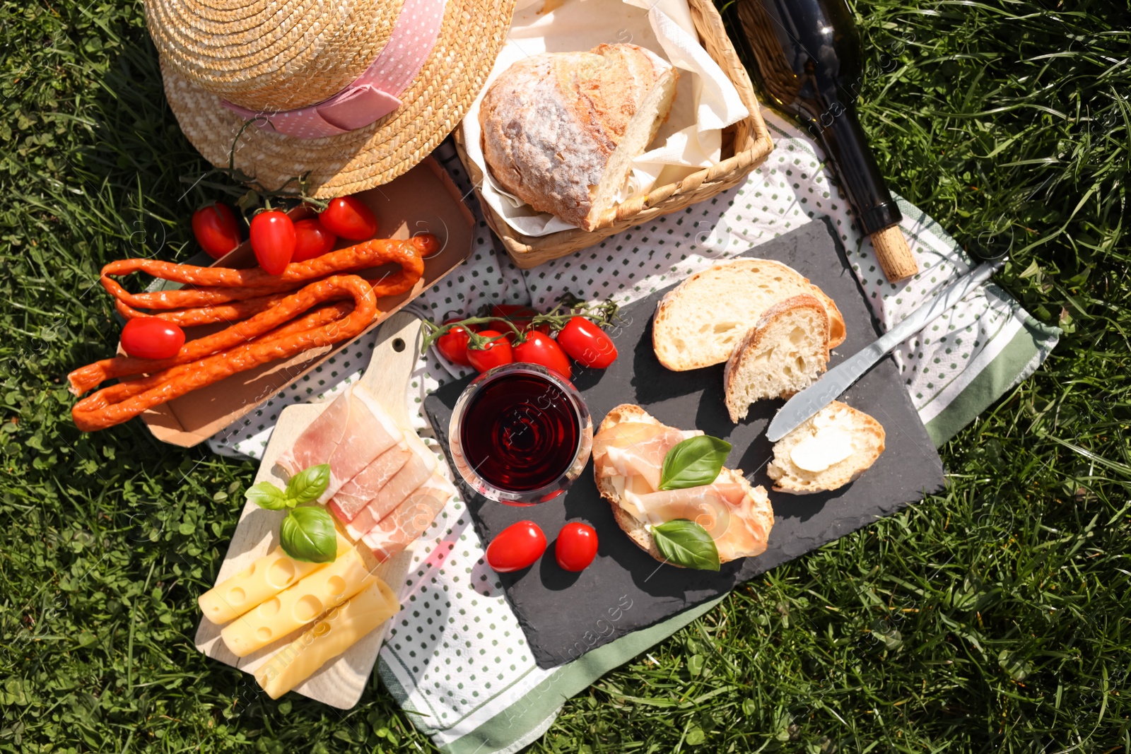 Photo of Blanket with wine and snacks for picnic on green grass, flat lay