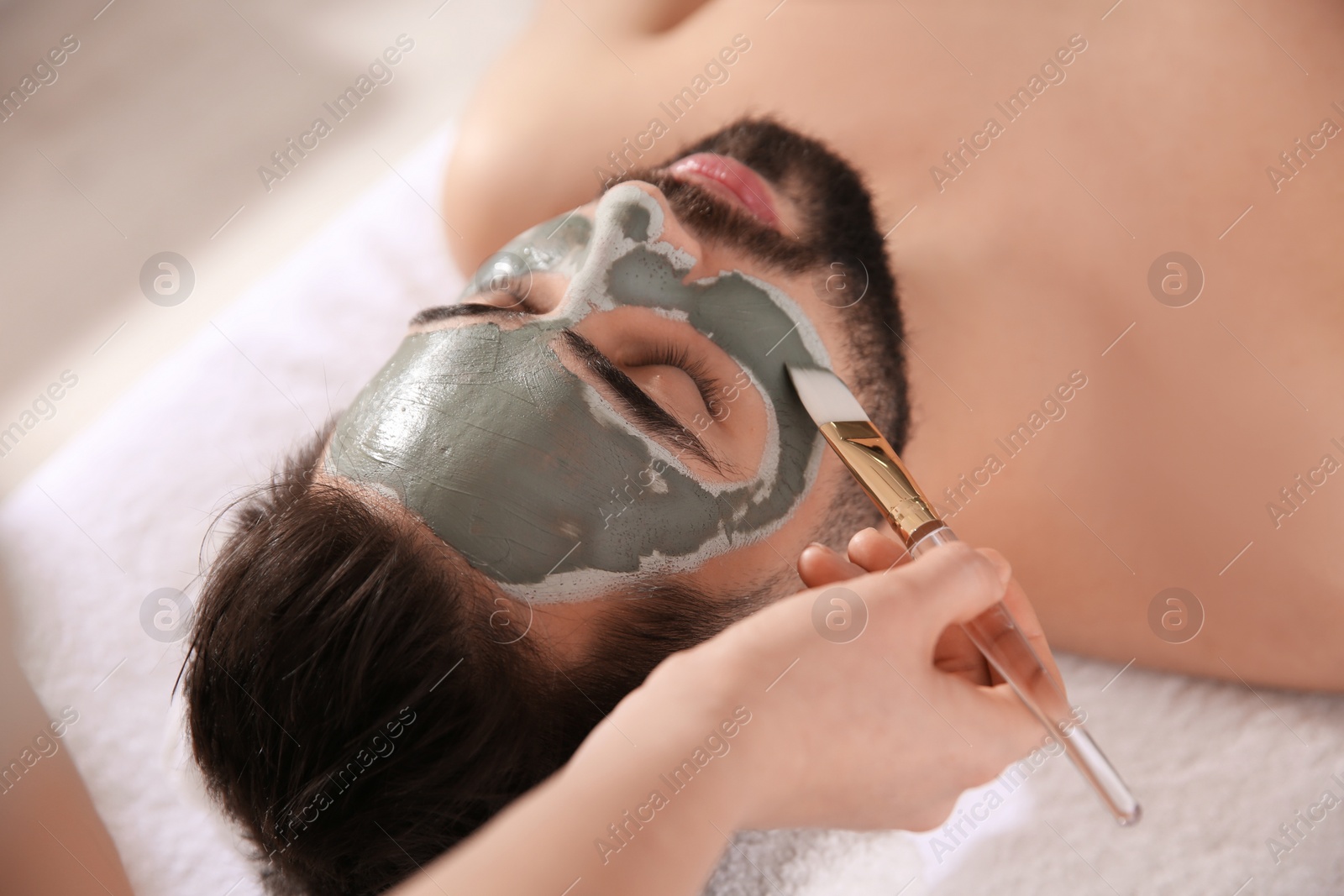 Photo of Cosmetologist applying mask on man's face in spa salon