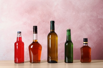 Bottles with different alcoholic drinks on table against color background