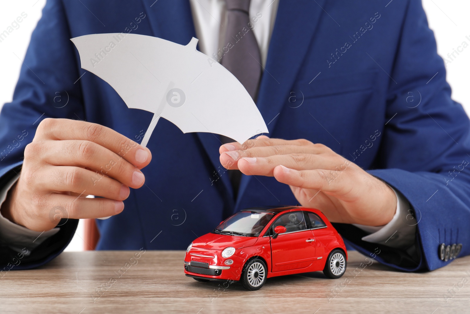 Photo of Insurance agent covering toy car with paper cutout umbrella and hand at table, closeup