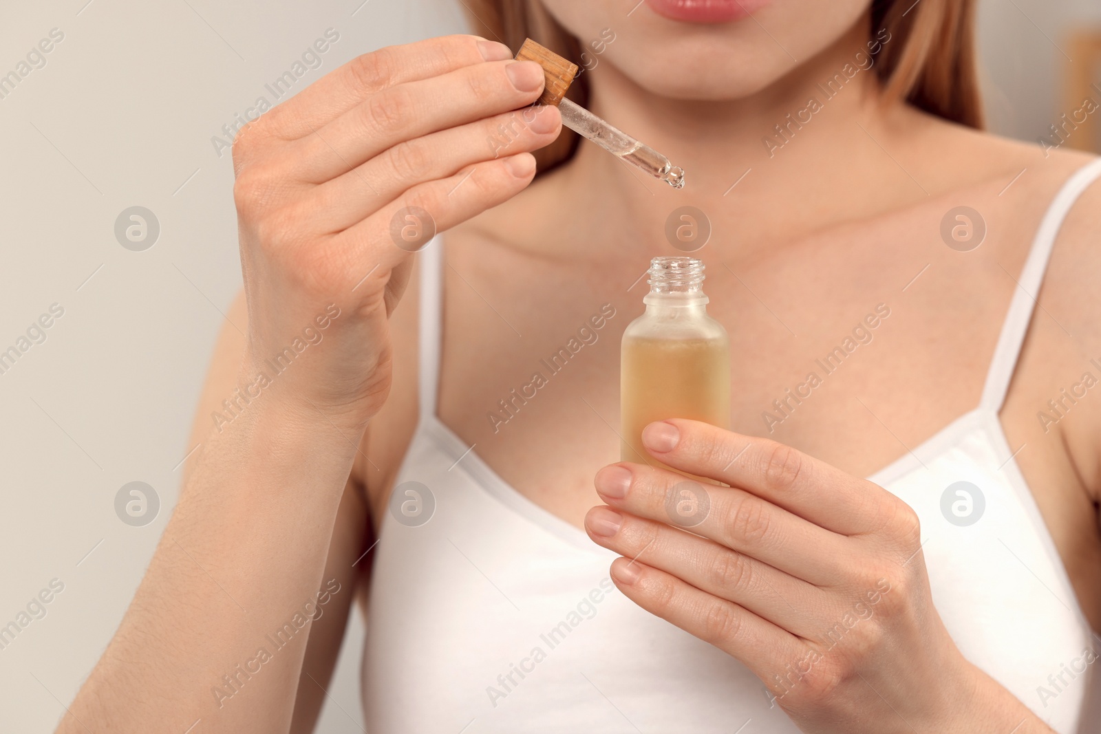 Photo of Woman with bottle of essential oil on blurred background, closeup
