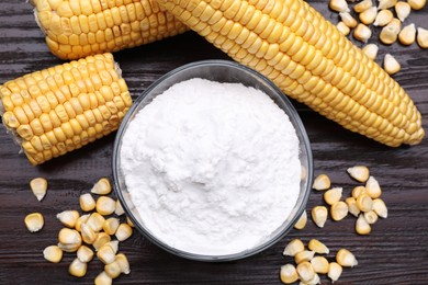 Photo of Bowl with corn starch, ripe cobs and kernels on dark wooden table, flat lay