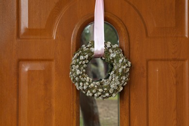 Photo of Wreath made of beautiful willow branches hanging on wooden door