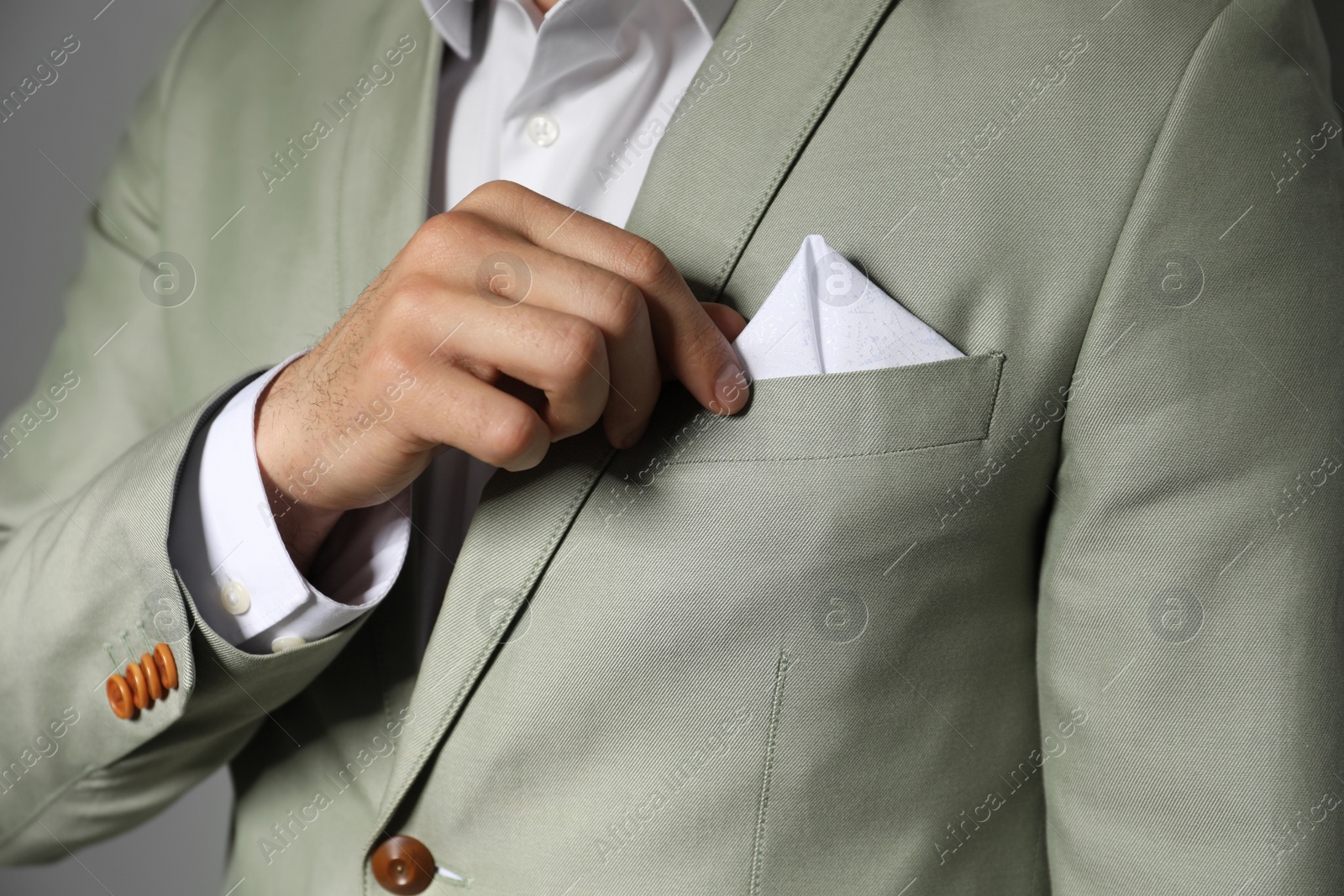 Photo of Man fixing handkerchief in breast pocket of his suit on grey background, closeup