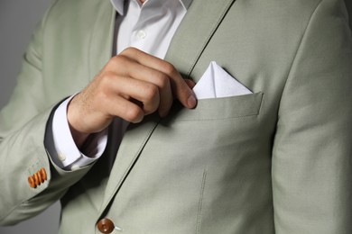 Photo of Man fixing handkerchief in breast pocket of his suit on grey background, closeup