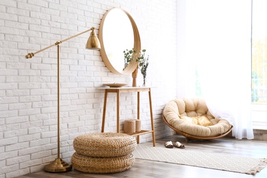 Photo of Hallway interior with big round mirror, table and decor near brick wall