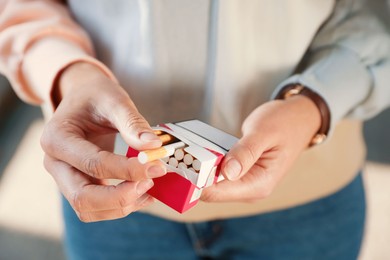 Woman taking cigarette out of pack outdoors, closeup