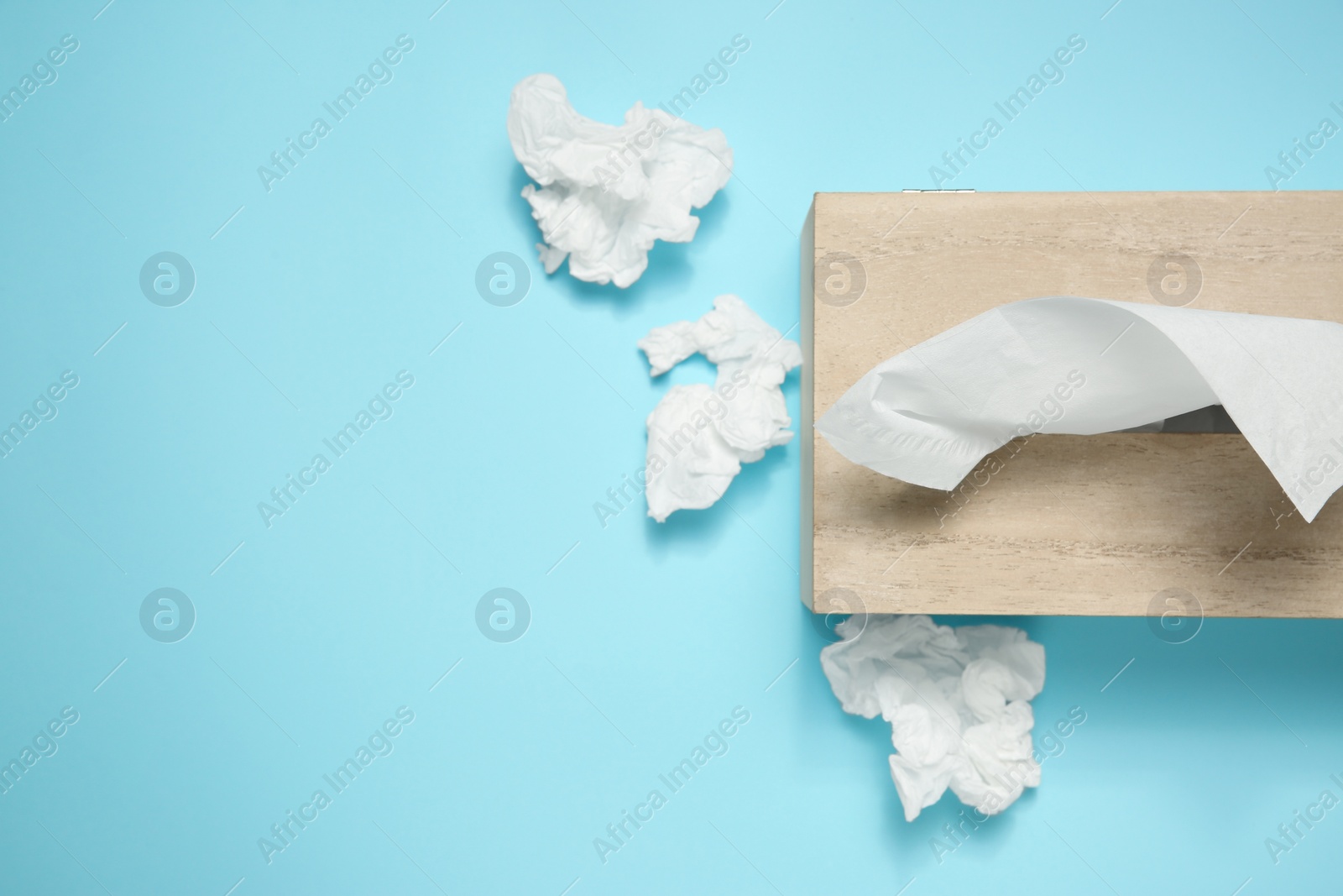 Photo of Used paper tissues and wooden holder on light blue background, flat lay. Space for text