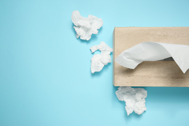 Used paper tissues and wooden holder on light blue background, flat lay. Space for text